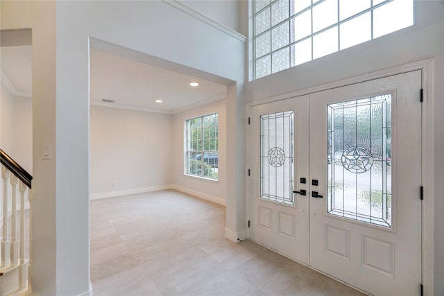 entrance foyer with ornamental molding, a towering ceiling, and french doors