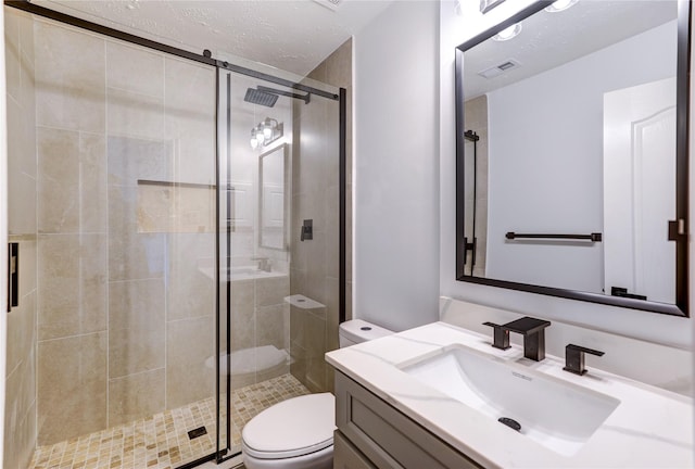 bathroom with vanity, a textured ceiling, a shower with door, and toilet