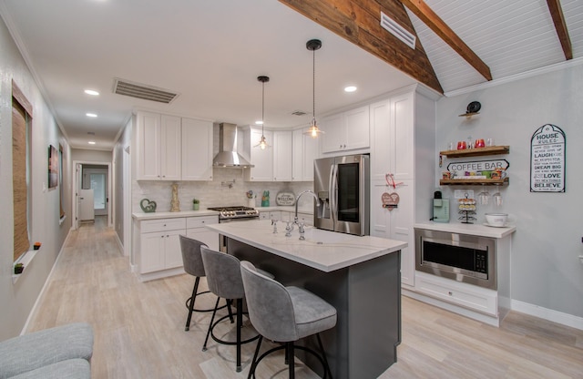 kitchen featuring white cabinets, decorative backsplash, hanging light fixtures, stainless steel appliances, and wall chimney range hood