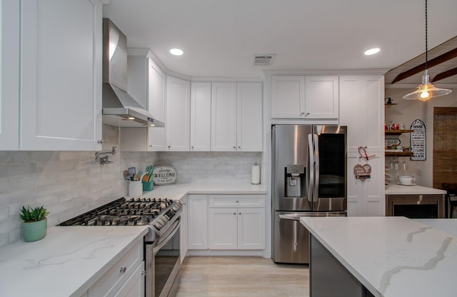 kitchen with white cabinetry, light stone counters, appliances with stainless steel finishes, pendant lighting, and wall chimney range hood