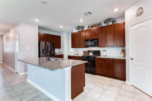 kitchen with sink, backsplash, light tile patterned floors, black appliances, and a center island with sink