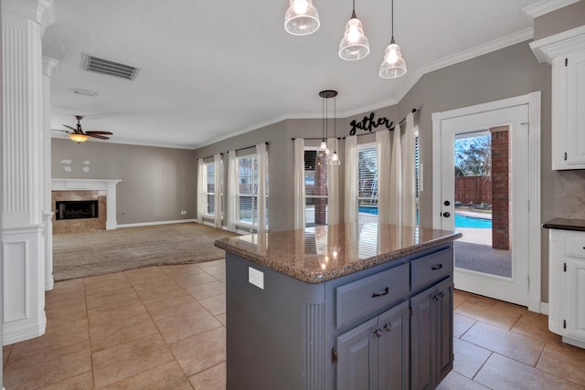 kitchen with a kitchen island, white cabinets, dark stone counters, hanging light fixtures, and a healthy amount of sunlight