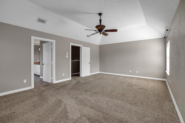 unfurnished bedroom with lofted ceiling, ensuite bathroom, dark colored carpet, a spacious closet, and ceiling fan