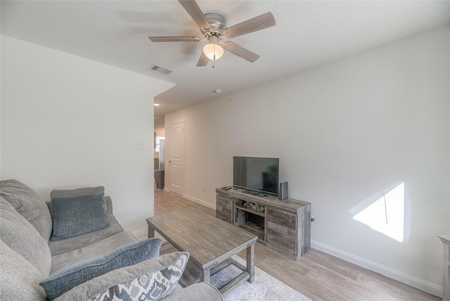 living room with light wood-style flooring, a ceiling fan, visible vents, and baseboards