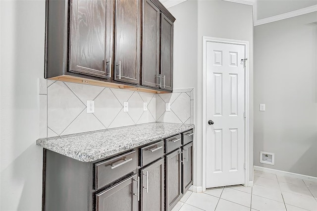 kitchen featuring dark brown cabinetry, light tile patterned floors, ornamental molding, light stone countertops, and backsplash