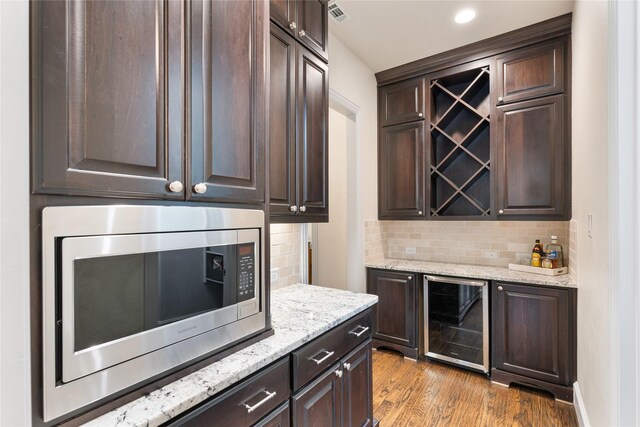 bar with stainless steel microwave, wine cooler, dark brown cabinetry, and light hardwood / wood-style flooring