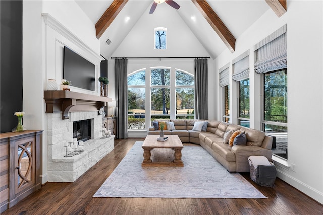 living room featuring a stone fireplace, dark hardwood / wood-style floors, high vaulted ceiling, ceiling fan, and beam ceiling