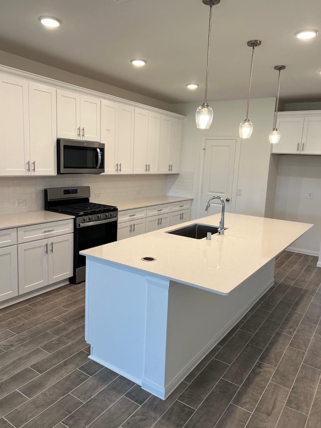 kitchen with wood finish floors, white cabinetry, backsplash, appliances with stainless steel finishes, and a sink