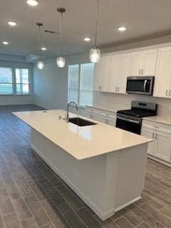 kitchen with white cabinets, a center island with sink, appliances with stainless steel finishes, pendant lighting, and a sink