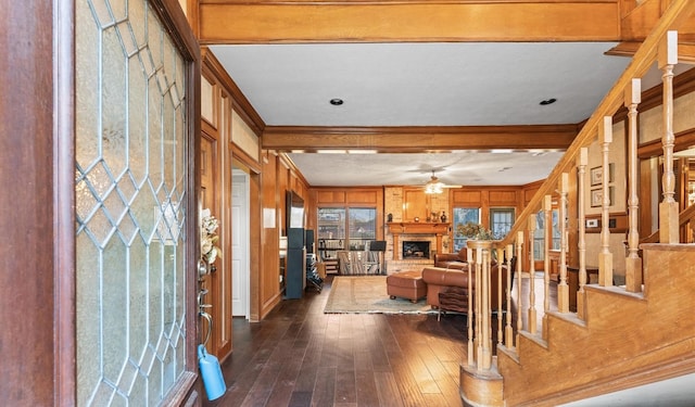 interior space with dark hardwood / wood-style floors, ceiling fan, crown molding, a brick fireplace, and beam ceiling