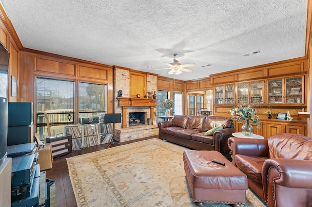 living room with wood walls, ornamental molding, ceiling fan, a brick fireplace, and dark wood-type flooring