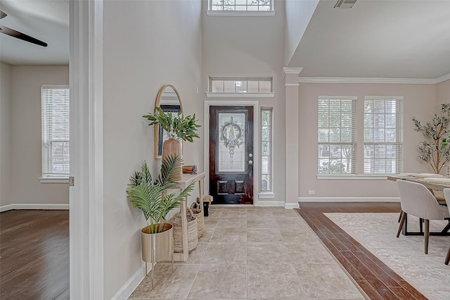 entryway featuring ornamental molding, a towering ceiling, a wealth of natural light, and light hardwood / wood-style floors