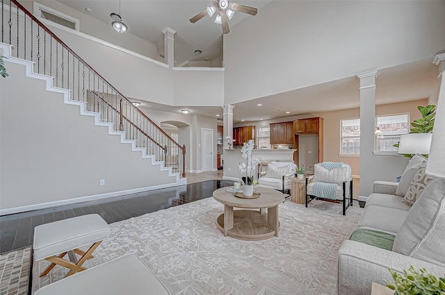 living room with ceiling fan, a high ceiling, light hardwood / wood-style flooring, and ornate columns