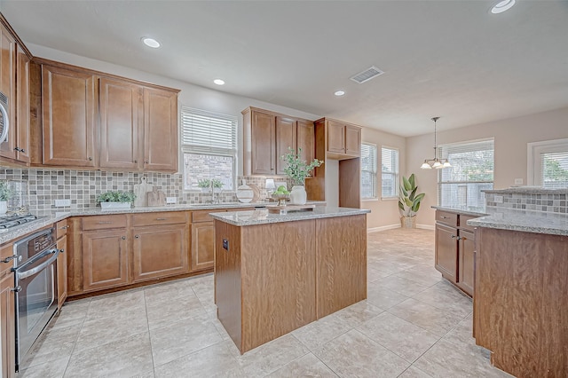 kitchen with sink, a kitchen island, pendant lighting, stainless steel appliances, and light stone countertops