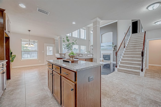 kitchen featuring light tile patterned flooring, decorative columns, hanging light fixtures, a center island, and light stone counters