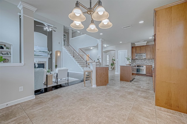 kitchen with appliances with stainless steel finishes, decorative columns, a tiled fireplace, a center island, and ceiling fan