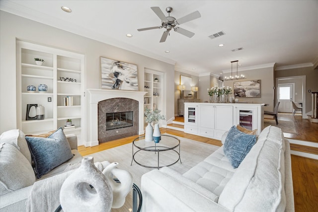 living room with a fireplace, ceiling fan, light hardwood / wood-style floors, crown molding, and built in shelves