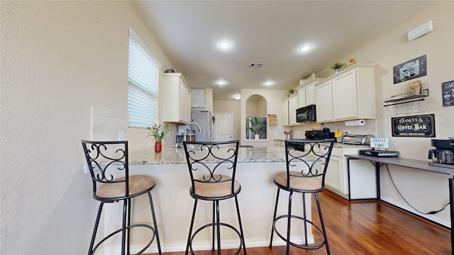 kitchen featuring white cabinetry, a kitchen breakfast bar, light stone countertops, and kitchen peninsula