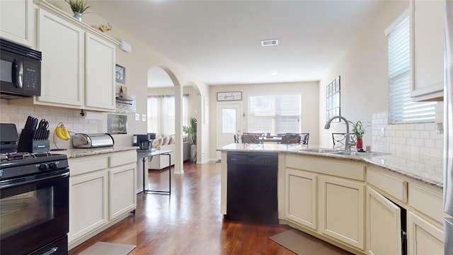 kitchen with sink, backsplash, black appliances, light stone countertops, and dark wood-type flooring