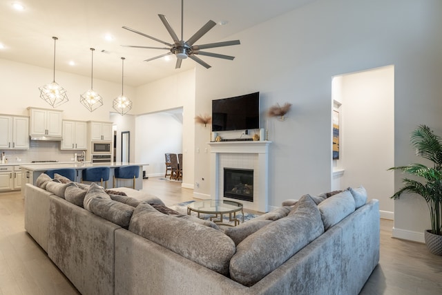 living room featuring ceiling fan, a tiled fireplace, light hardwood / wood-style flooring, and a towering ceiling