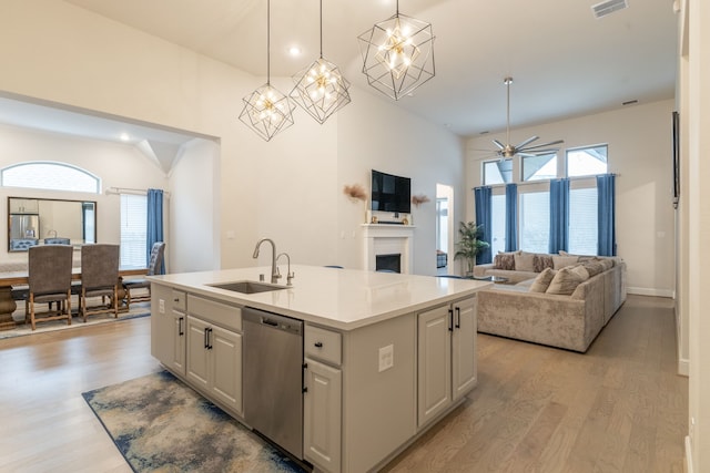 kitchen featuring sink, dishwasher, hanging light fixtures, a center island with sink, and light wood-type flooring