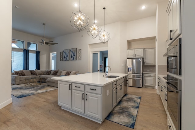 kitchen featuring appliances with stainless steel finishes, decorative light fixtures, white cabinetry, an island with sink, and sink