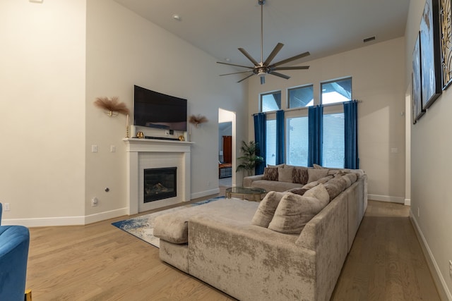 living room with ceiling fan, hardwood / wood-style floors, and a towering ceiling