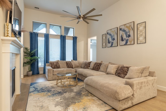 living room with ceiling fan, light hardwood / wood-style floors, and a towering ceiling