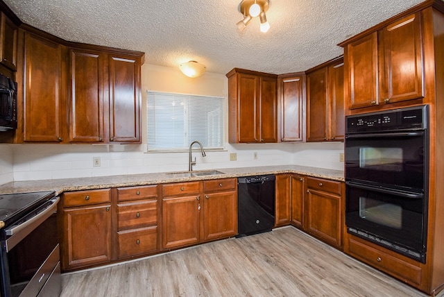 kitchen featuring sink, a textured ceiling, light stone countertops, light hardwood / wood-style floors, and black appliances