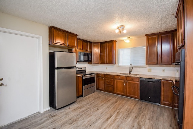 kitchen featuring sink, light stone counters, a textured ceiling, light wood-type flooring, and black appliances