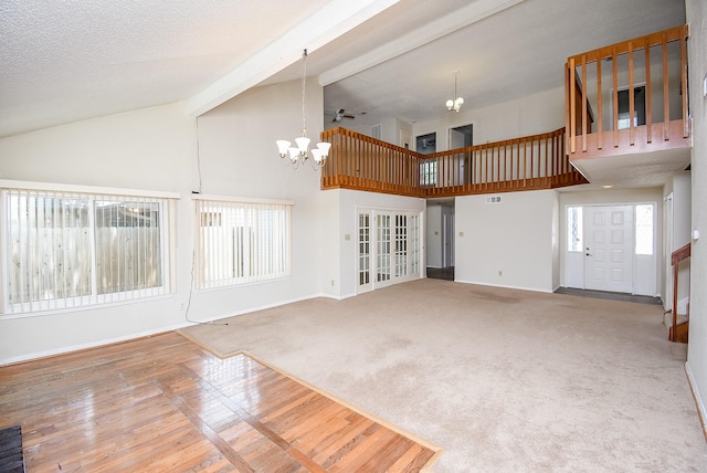 unfurnished living room with beam ceiling, high vaulted ceiling, carpet flooring, a textured ceiling, and ceiling fan with notable chandelier