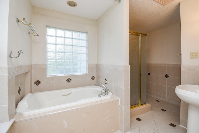 bathroom featuring plus walk in shower, sink, tile walls, tile patterned floors, and a textured ceiling