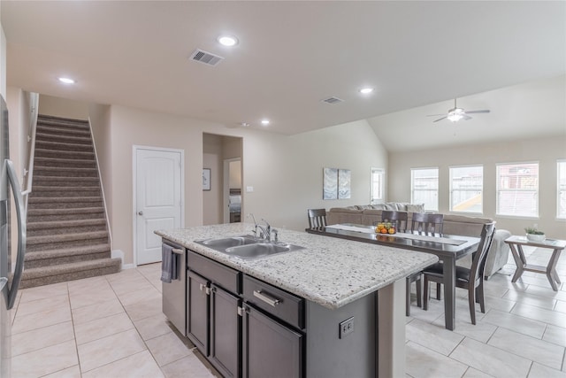 kitchen with sink, light tile patterned floors, dishwasher, light stone countertops, and a center island with sink