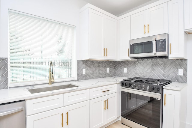 kitchen with sink, appliances with stainless steel finishes, white cabinetry, light stone counters, and tasteful backsplash