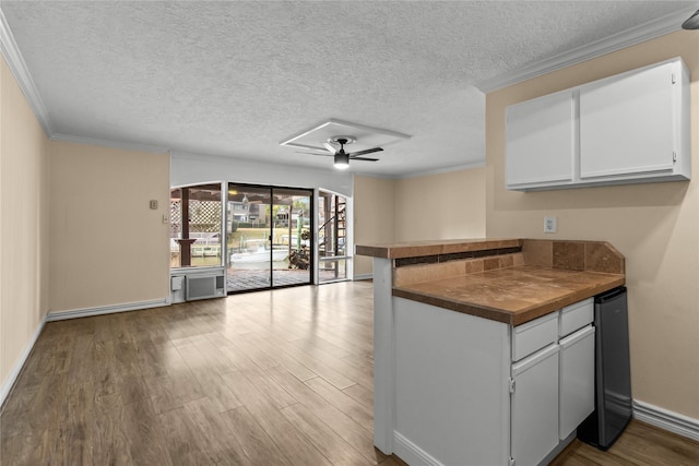 kitchen with hardwood / wood-style flooring, ceiling fan, white cabinetry, ornamental molding, and kitchen peninsula