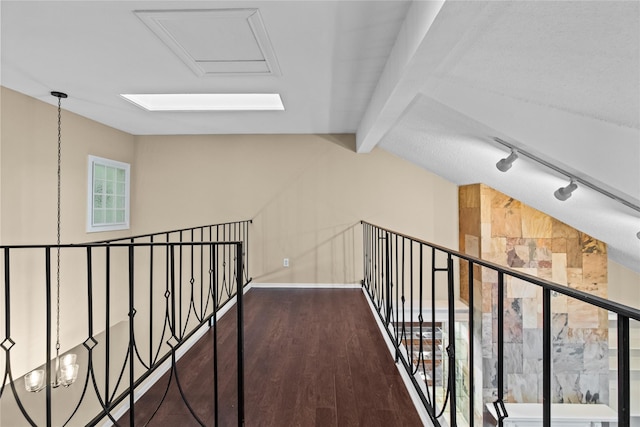 hall with dark hardwood / wood-style flooring, rail lighting, and vaulted ceiling with beams