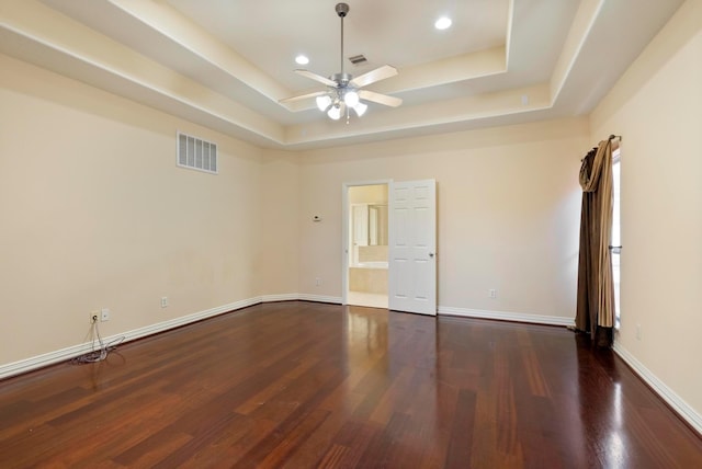 empty room with a raised ceiling, dark wood-type flooring, and ceiling fan