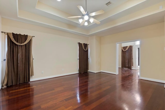 unfurnished room with a tray ceiling, dark wood-type flooring, and ceiling fan