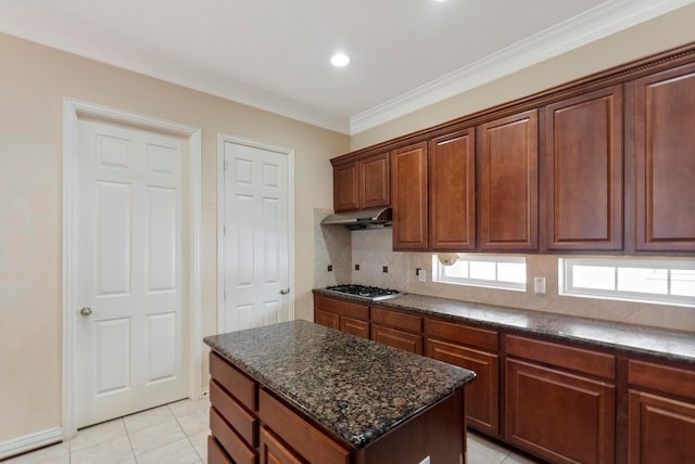 kitchen with a center island, stainless steel gas cooktop, light tile patterned flooring, decorative backsplash, and dark stone counters