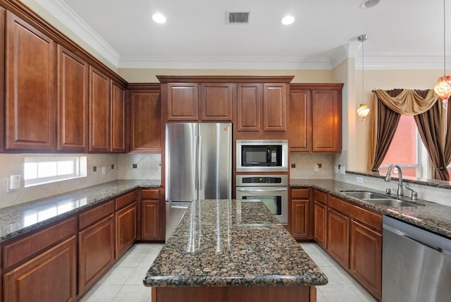 kitchen featuring sink, decorative light fixtures, appliances with stainless steel finishes, a kitchen island, and dark stone counters