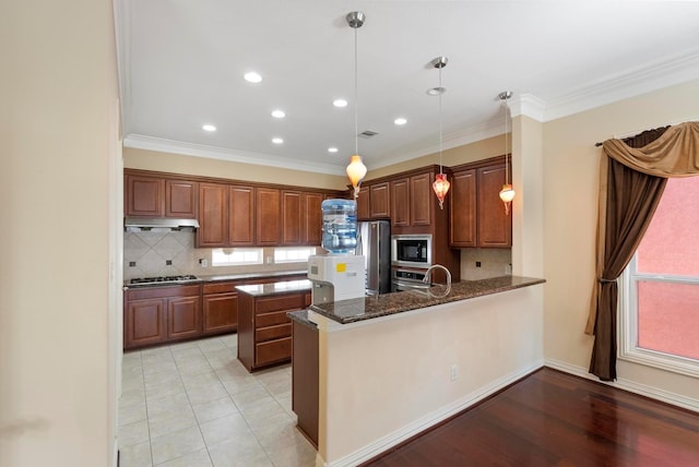 kitchen featuring appliances with stainless steel finishes, backsplash, dark stone counters, hanging light fixtures, and kitchen peninsula