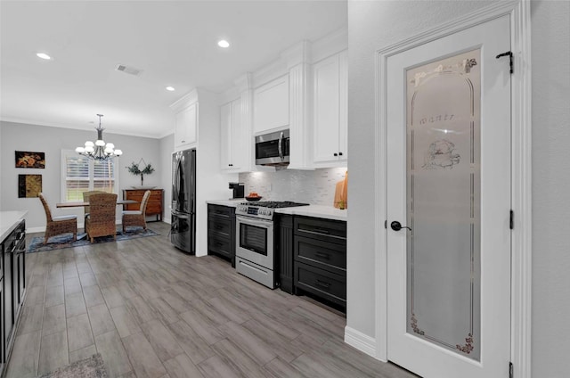 kitchen featuring appliances with stainless steel finishes, decorative light fixtures, white cabinetry, decorative backsplash, and crown molding