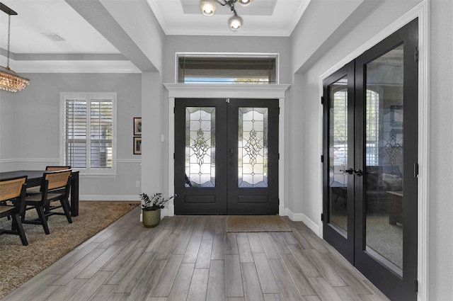 foyer entrance with french doors, ornamental molding, a chandelier, and light hardwood / wood-style flooring