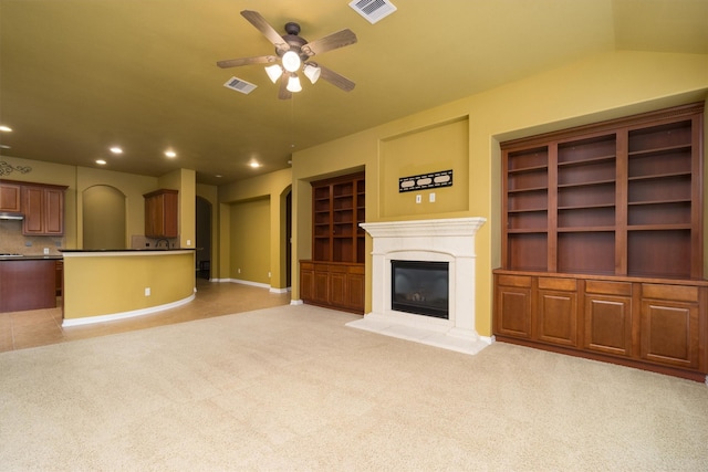 unfurnished living room featuring light colored carpet, ceiling fan, and built in shelves