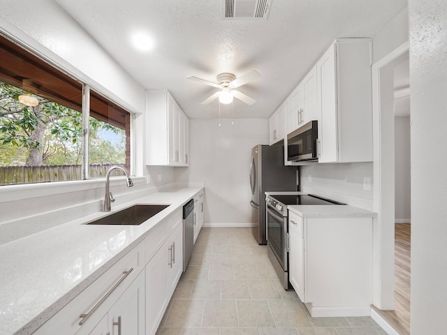 kitchen with sink, ceiling fan, appliances with stainless steel finishes, white cabinetry, and light stone counters