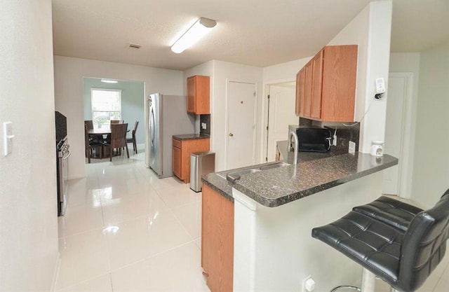 kitchen with a breakfast bar, light tile patterned floors, appliances with stainless steel finishes, kitchen peninsula, and dark stone counters