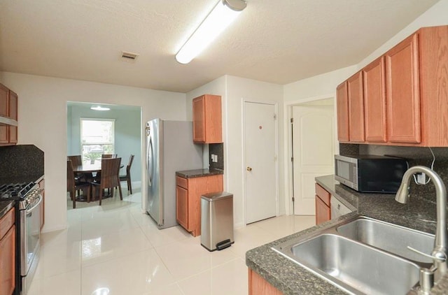 kitchen featuring appliances with stainless steel finishes, sink, light tile patterned floors, and a textured ceiling