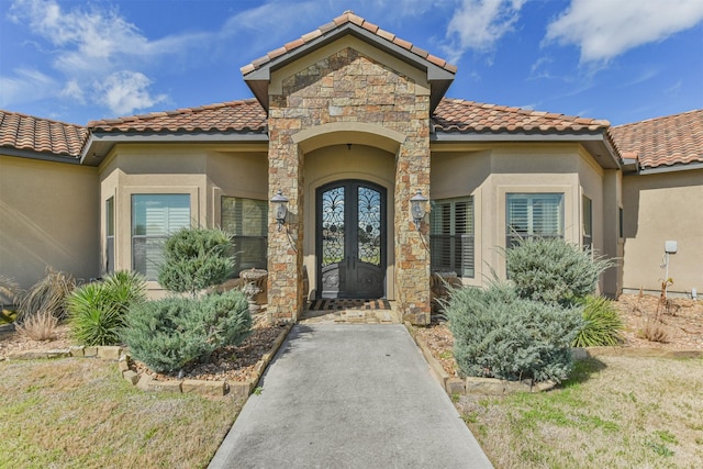 view of exterior entry featuring stone siding, french doors, a lawn, and stucco siding