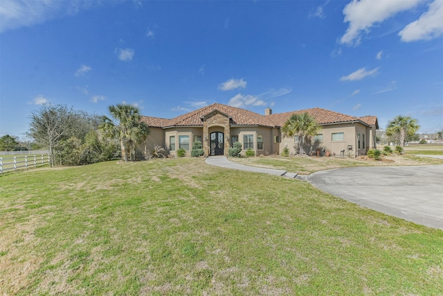 mediterranean / spanish house featuring fence, a tiled roof, stucco siding, a chimney, and a front yard