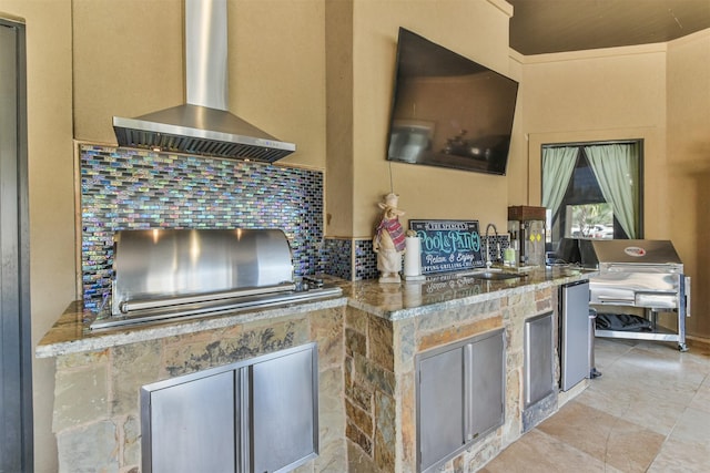 kitchen with light tile patterned floors, a sink, light stone countertops, wall chimney exhaust hood, and tasteful backsplash